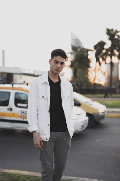 A vertical shot of a young stylish caucasian man in a white jacket posing outdoors - 写真・画像