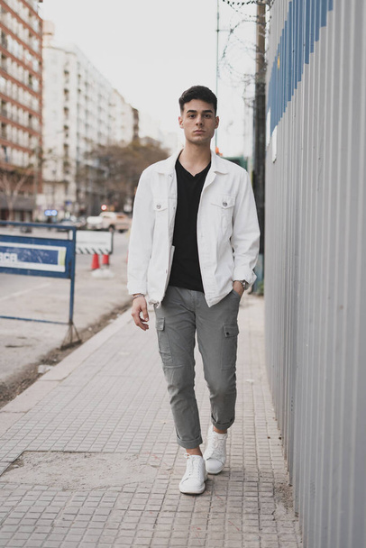 A vertical shot of a young stylish male in a white t-shirt posing on the street - Zdjęcie, obraz
