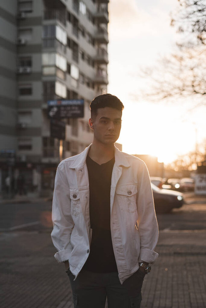 A vertical shot of a young stylish caucasian man in a white jacket posing outdoors - Zdjęcie, obraz