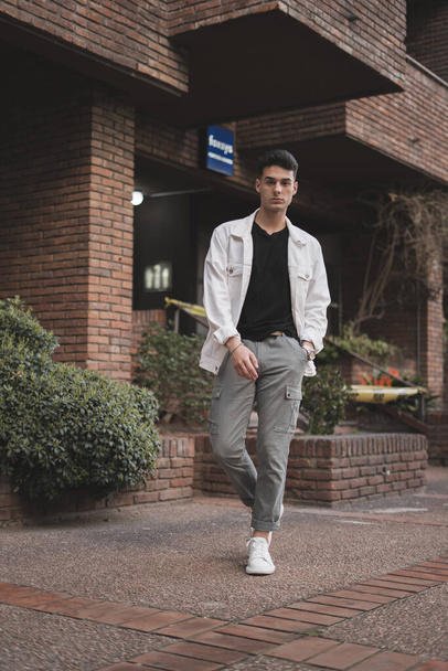 A vertical shot of a young stylish Caucasian male posing near a brick building - Foto, afbeelding