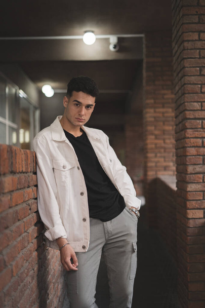 A vertical shot of a young stylish Caucasian male posing by a brick wall - 写真・画像