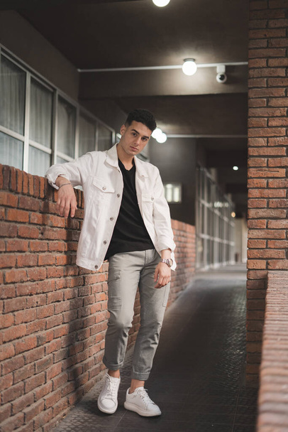 A vertical shot of a young stylish Caucasian male posing by a brick wall - Fotó, kép