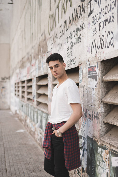 A vertical shot of a young stylish male in a white t-shirt posing on the street - Foto, immagini