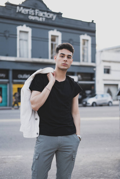 A vertical shot of a young stylish male in a white t-shirt posing on the street - Zdjęcie, obraz