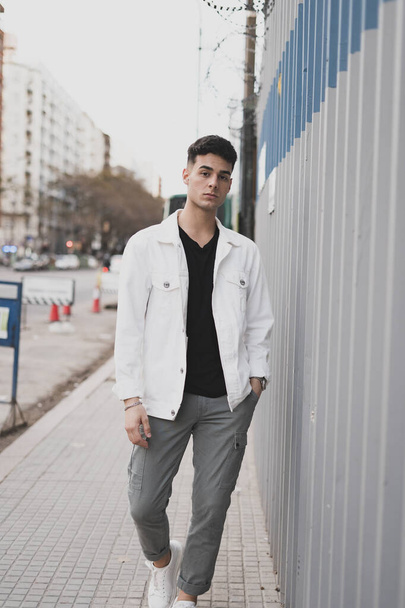 A vertical shot of a young stylish caucasian man in a white jacket outdoors - Fotografie, Obrázek