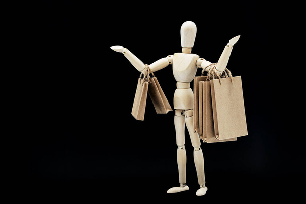 Sale or shopping concept, in minimalism style. Wooden puppet with craft paper shopping bags on black background. - Фото, зображення