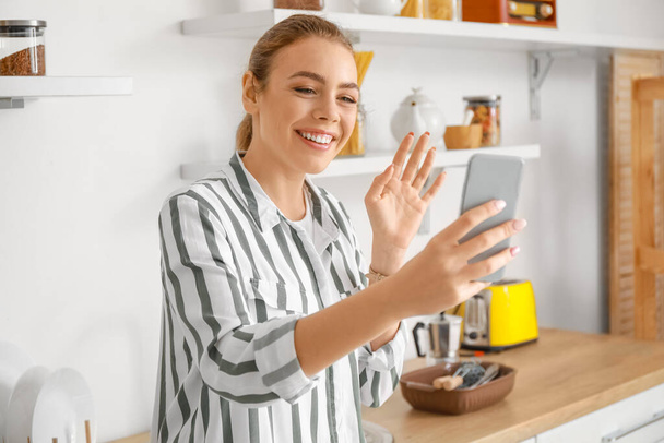 Cep telefonlu genç bir kadın mutfakta görüntülü sohbet ediyor. - Fotoğraf, Görsel