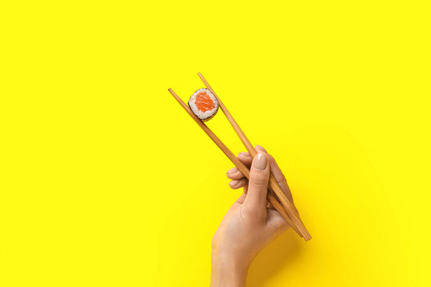 Woman holding chopsticks with delicious maki roll on color background - Photo, Image