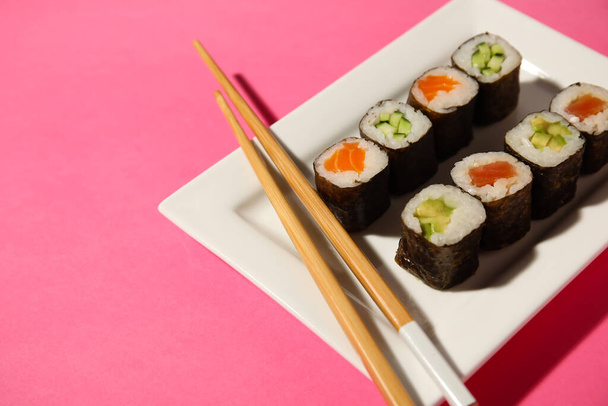 Πιάτο με διάφορα maki rolls και ξύλινα chopsticks στο φόντο χρώμα, closeup - Φωτογραφία, εικόνα