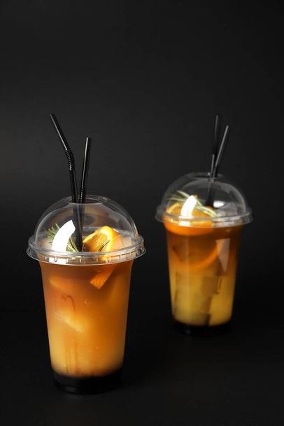 Plastic kopjes lekkere koffie met sinaasappelsap op donkere achtergrond - Foto, afbeelding