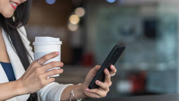 Une femme d'affaires boit du café et utilise un smartphone pour communiquer et vérifier le travail de la maison en ligne parce qu'elle démarre une entreprise qui peut commander et vérifier de n'importe où en ligne. - Photo, image