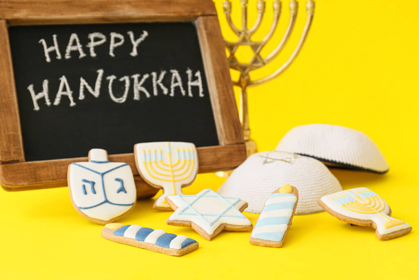 Leckere Plätzchen, jüdische Hüte und Kreidetafel mit dem Text HAPPY HANUKKAH auf farbigem Hintergrund - Foto, Bild