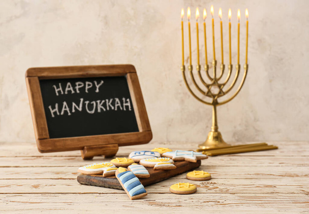 Tasty cookies, menorah and chalkboard with text HAPPY HANUKKAH on table - Photo, Image