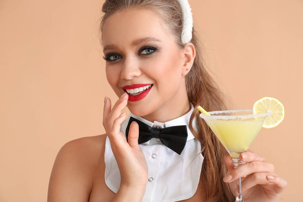 Νεαρή γυναίκα ντυμένη σέξι σερβιτόρα με κοκτέιλ στο φόντο χρώμα - Φωτογραφία, εικόνα