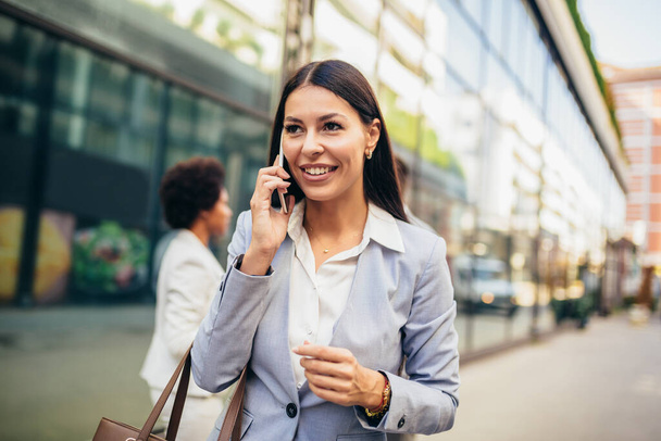 Portret pięknej uśmiechniętej kobiety w modzie biuro ubrania rozmawiając na telefon stojąc na zewnątrz. - Zdjęcie, obraz