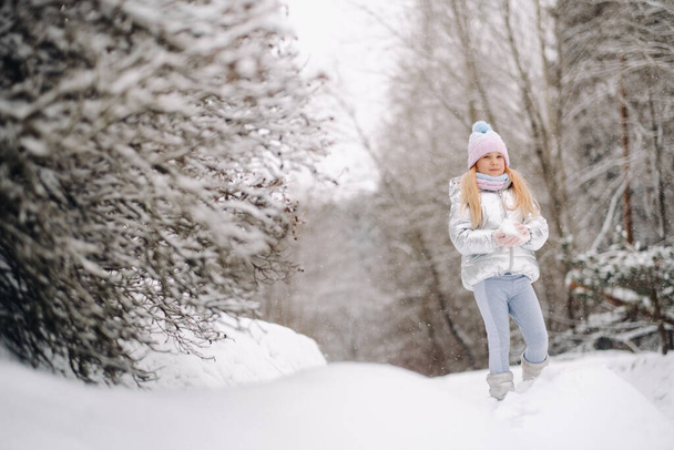a little girl in a silver jacket in winter goes outside in winter. - Foto, Imagem
