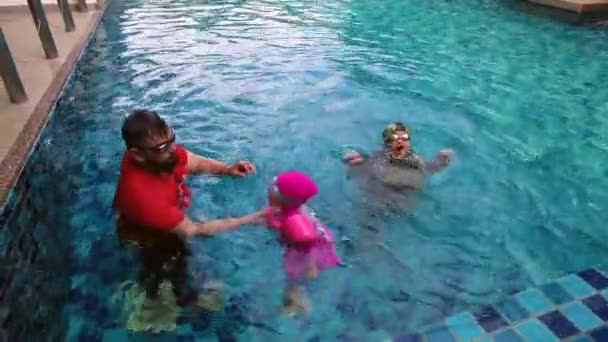 Korkea kulma näkymä Aasian perheen hauskaa uima-altaassa ulkona. Aktiivisia lapsia. Kuvamateriaali voi sisältää heikosta valosta johtuvaa melua. - Materiaali, video