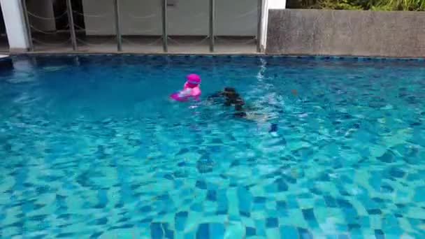 Veli ja lapsi sisko leikkivät yhdessä uima-altaassa. Aktiiviset lapset pitävät hauskaa yhdessä. Kuvamateriaali voi sisältää heikosta valosta johtuvaa melua. - Materiaali, video