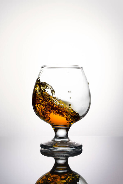 Splash of cognac in glass isolated on a light background - Fotoğraf, Görsel