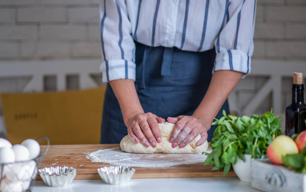 Cook hands kneading dough, piece of dough with white wheat flour. Low key shot, close up on hands, some ingredients around on table. - Φωτογραφία, εικόνα