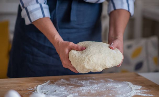 Cook hands kneading dough, piece of dough with white wheat flour. Low key shot, close up on hands, some ingredients around on table. - Photo, image
