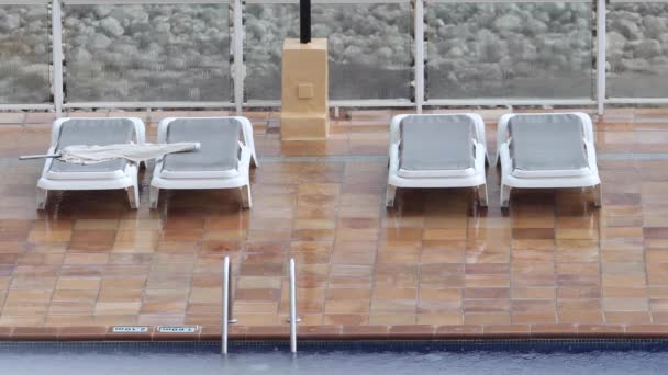 Clima extremadamente lluvioso en un complejo vacacional que muestra la lluvia derramándose sobre tumbonas vacías al lado de una piscina de hotel en la isla española de Ibiza en España - Metraje, vídeo