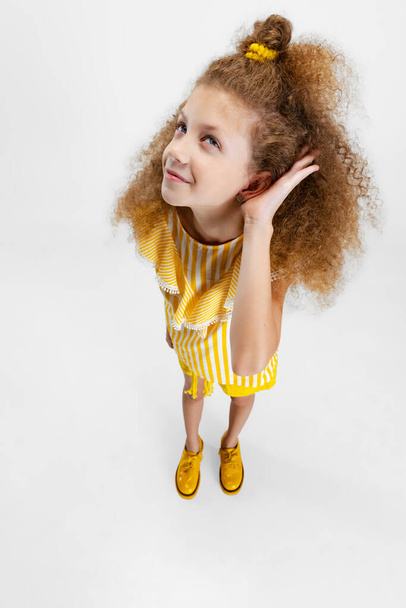 Close-up portrait of little cute curly girl, child listening to secrets, news with her hand to ear isolated over white studio background. - Foto, Imagem