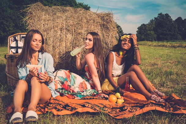 multi-etnische meisjes met picknick in de buurt van stapel op een veld  - Foto, afbeelding