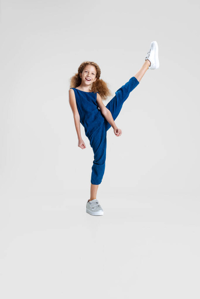 One little Caucasian cute girl in blue stylish jumpsuit having fun isolated over white studio background. Leisure activity concept - Photo, image