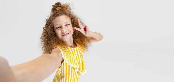 Front camera view of little smiling curly beautiful girl looking at camera isolated over white studio background. - Φωτογραφία, εικόνα