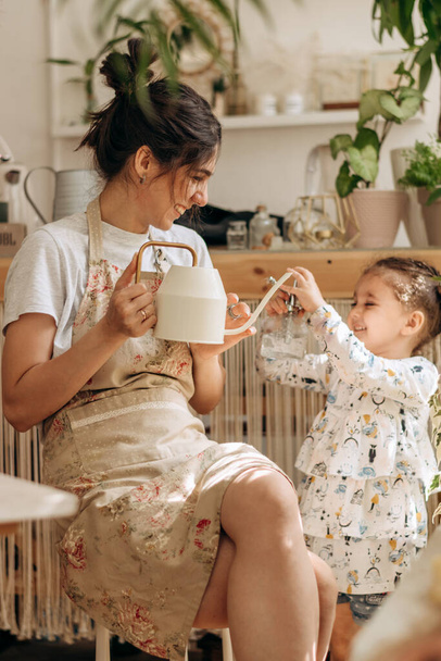 Mixed race family woman and her little daughter is watering houseplants at home and having fun splashing water.Home gardening.Family leisure,hobby concept.Biophilia design and urban jungle concept - Photo, image