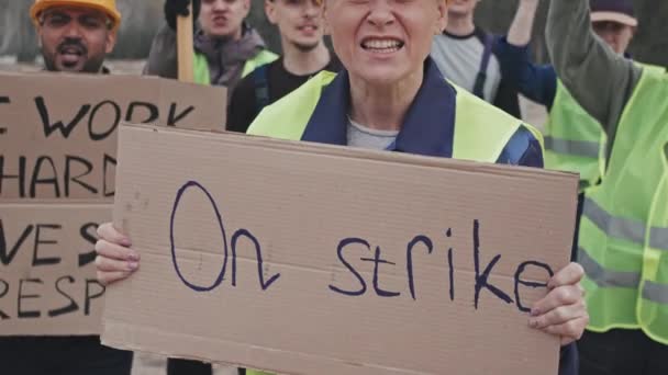 Középső rész közeli felvétel dühös női munkásokról és más munkásokról, akik jeleket tartanak és kántálnak, miközben a szabadban tüntetnek. - Felvétel, videó