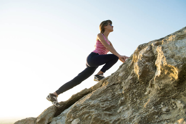 Mujer excursionista escalando empinada roca grande en un día soleado. Joven escaladora supera difícil ruta de escalada. Recreación activa en concepto de naturaleza. - Foto, imagen
