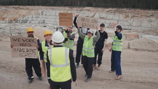 Langzame tracking shot van menigte van steengroeve werknemers met borden protesteren en confronteren corporate manager buiten - Video