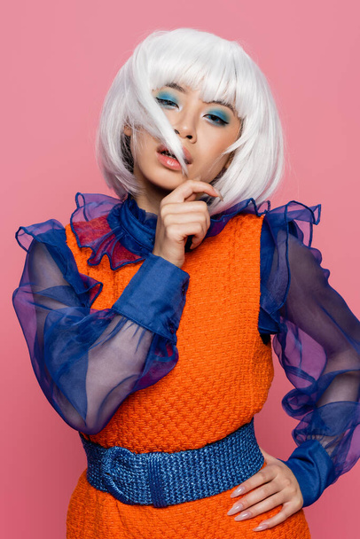 Stílusos ázsiai pop art modell megható haj és nézi kamera elszigetelt rózsaszín  - Fotó, kép