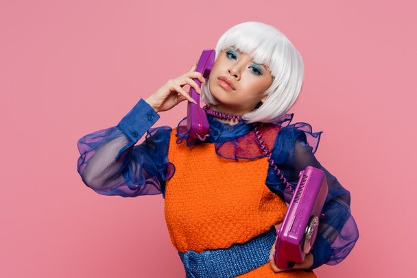 Pretty asian pop art model wrapped in cable talking on telephone isolated on pink  - Photo, image