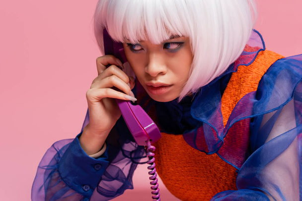 Modèle pop art asiatique parlant sur téléphone rétro avec câble sur fond rose  - Photo, image