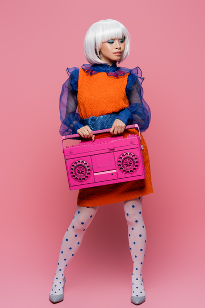 Trendy asian woman in vintage dress holding boombox on pink background - Valokuva, kuva