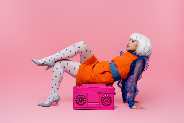 Stylish asian woman in retro dress and white wig posing near boombox on pink background - Photo, Image