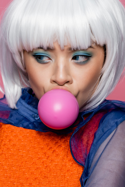 Portrait of asian pop art model in white wig blowing bubble gum isolated on pink  - Фото, изображение