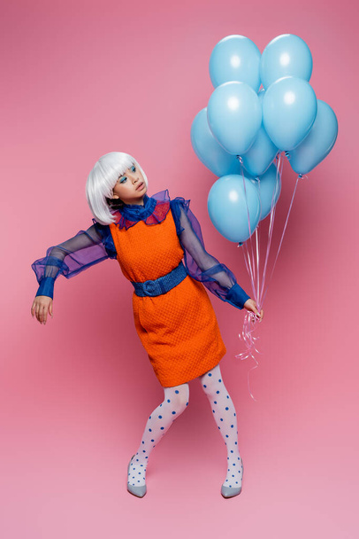 Asian pop art model holding blue balloons on pink background - Foto, afbeelding
