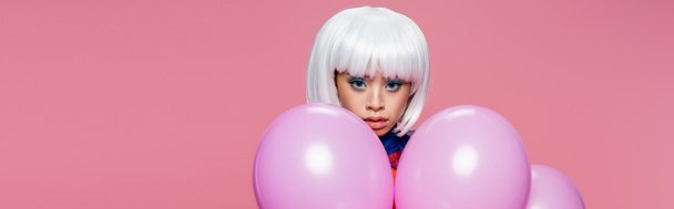 Asian woman in white wig looking at camera near balloons isolated on pink, banner  - 写真・画像