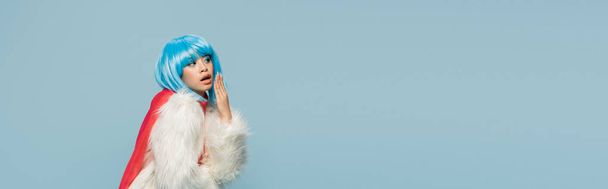 Astonished asian woman in wig and furry jacket looking away isolated on blue, banner  - Foto, Imagem
