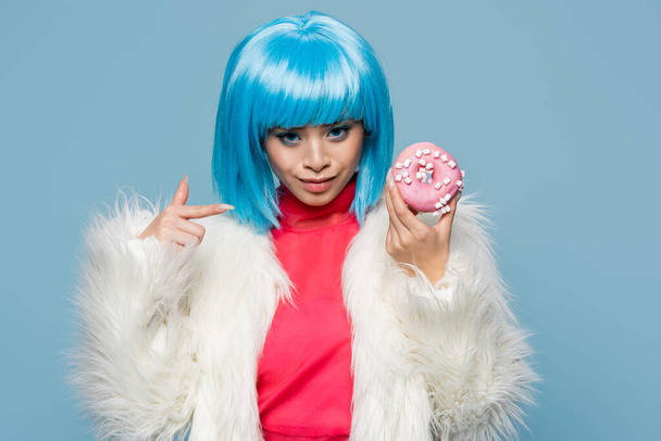 sonriente asiático mujer en pop arte estilo apuntando a donut aislado en azul  - Foto, Imagen