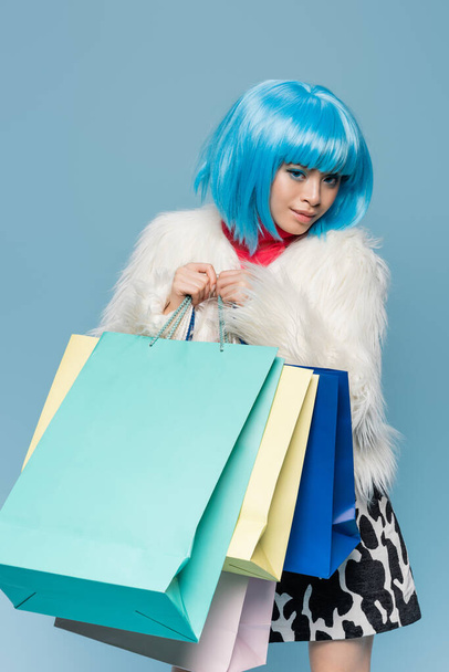 Junge Asiatin in heller Perücke mit Einkaufstüten auf blauem Grund  - Foto, Bild