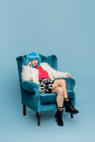 Asian woman in pop art style sitting on armchair on blue background  - 写真・画像