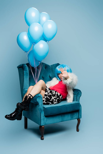 Азиатка в поп-арте держит воздушные шары и прикрывает лицо рукой на синем фоне  - Фото, изображение