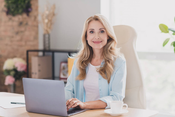 Foto portret glimlachende vrolijke zakenvrouw zitten aan tafel typen bericht op laptop - Foto, afbeelding
