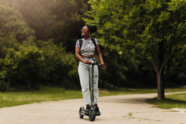 Hermosa mujer feliz en un scooter eléctrico para trabajar, chica moderna, nueva generación, transporte eléctrico, ecología, transporte ecológico, puesta de sol - Foto, Imagen