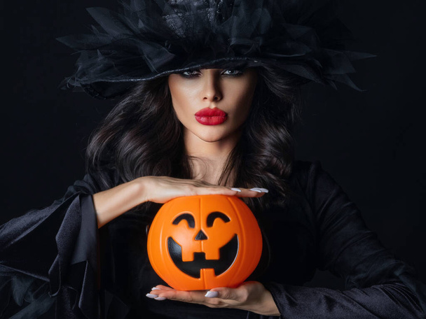 Kobieta w stroju czarownicy trzymać Halloween dyni kosz na cukierki na czarnym tle - Zdjęcie, obraz